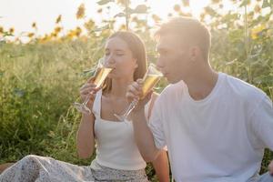 jovem casal fazendo piquenique no campo de girassol ao pôr do sol foto