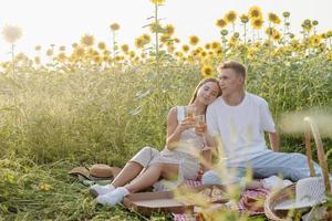 jovem casal fazendo piquenique no campo de girassol ao pôr do sol foto