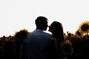 lindo casal caminhando juntos em campos de girassóis ao pôr do sol foto