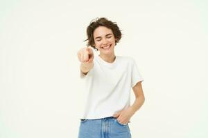 retrato do excitado, sorridente jovem mulher, apontando dedo às Câmera, convidativo você, parabenizando, em pé sobre branco estúdio fundo foto