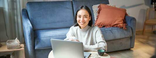 trabalhos a partir de lar, freelance e e-learning conceito. jovem mulher estudo, sentado dentro frente do computador portátil, trabalhando em controlo remoto, local de trabalho dentro vivo quarto foto