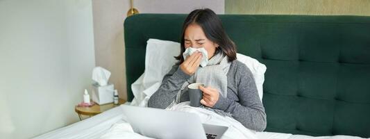 mulher com frio, tendo gripe, ficando dentro cama, espirros dentro guardanapo, escorrendo nariz e gripe sintomas foto