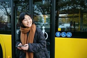 retrato do coreano menina olhando para dela ônibus em uma parar, segurando Móvel telefone, verificação agendar, Tempo mesa em Smartphone aplicativo foto