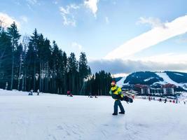 homem com snowboard e chapéu vermelho de Natal subindo pela colina coberta de neve foto