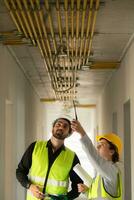 masculino e fêmea engenheiros trabalhando em construção site, elas estão monitoramento a edifício de elétrico sistema. foto