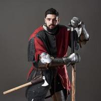 cavaleiro medieval em fundo cinza. retrato de guerreiro brutal com rosto sujo com cota de malha, roupas vermelhas e pretas e machado de batalha foto