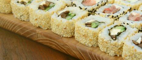 close-up de muitos rolos de sushi com recheios diferentes estão sobre uma superfície de madeira. tiro macro de comida japonesa clássica cozida com um espaço de cópia foto