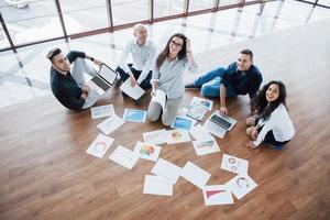 estratégia de planejamento em conjunto. equipe de negócios olhando papéis no chão com o gerente apontando para uma ideia. cooperação realização corporativa. planejamento desenho desenho. conceito de trabalho em equipe foto