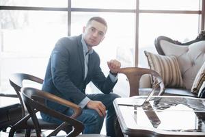 jovem empresário trabalhando em um escritório moderno. homem vestindo camisa branca e usando laptop contemporâneo. fundo de janelas panorâmicas foto