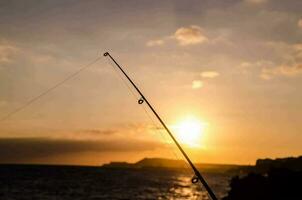 uma pescaria Cajado é dentro a primeiro plano do uma pôr do sol foto