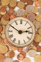 uma relógio cercado de moedas em uma branco fundo foto