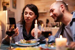 casal surfar em Internet usando Smartphone durante romântico jantar dentro cozinha. adultos sentado às a mesa dentro a cozinha navegando, procurando, usando smartphones, Internet, a comemorar aniversário. foto