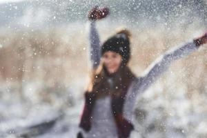 garota de inverno beleza soprando neve no parque de inverno gelado. ao ar livre. flocos de neve voando. dia ensolarado. retroiluminado. alegre beleza jovem se divertindo em winter park. desfocado