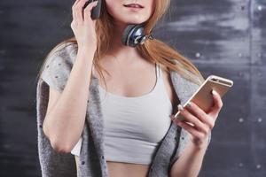 foto de uma jovem adorável loira com um sorriso fofo usando grandes fones de ouvido profissionais de monitoramento contra o fundo cinza do estúdio