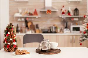 esvaziar natal decorado culinária cozinha com ninguém dentro isto pronto para Natal feriado. em mesa em pé cozido caseiro delicioso bolacha e copo do café esperando para tradicional manhã sobremesa foto