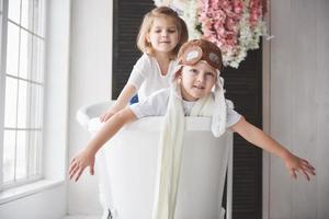 retrato de uma menina e um menino com chapéu de piloto, jogando no banheiro de pilotos ou marinheiros. o conceito de viagem, infância e a realização de sonhos foto