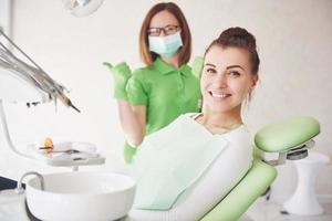 uma jovem está satisfeita com o trabalho do dentista e levanta o polegar