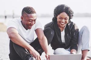 dois amigos felizes de alunos ou parceiros de negócios estão sentados ao ar livre e desfrutando de um laptop foto