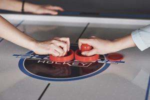 mãos de jovens segurando o atacante na mesa de air hockey na sala de jogos foto