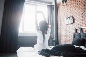 linda mulher negra acordando em sua cama, ela está sorrindo e se espreguiçando foto