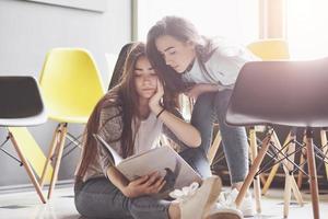 duas lindas gêmeas passam o tempo lendo um livro na biblioteca pela manhã. irmãs relaxando em um café e se divertindo juntas foto