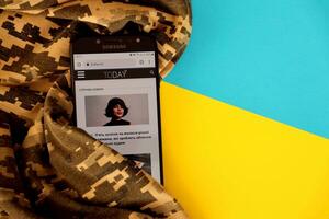 Kyiv, Ucrânia - 4 poderia, 2023 hoje ua ucraniano notícia portal em Smartphone tela com ucraniano bandeira e camuflar tecido foto
