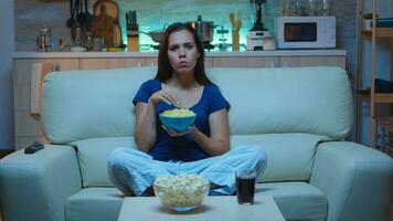 atento concentrado jovem senhora assistindo filme comendo lanches . chocado atônito casa sozinho às noite mulher com surpreso face olhando às suspense filme sentado em confortável sofá. foto