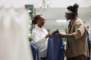 africano americano homem obtendo assistência a partir de roupas loja trabalhador enquanto selecionando jaqueta. compras Shopping cliente Perguntando assistente para Socorro enquanto escolhendo Novo equipamento dentro boutique foto