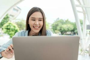 bela mulher asiática estudante animado verificando os resultados do teste de linguagem no laptop. sorriso menina feliz estudo online. livro no campus da faculdade. retrato feminino na universidade internacional da ásia foto