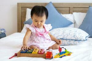 adorável pequeno ásia bebê criança pequena é sentado em a cama jogando de madeira melodia brinquedo para pré escola Aprendendo e crescimento desenvolvimento conceito foto