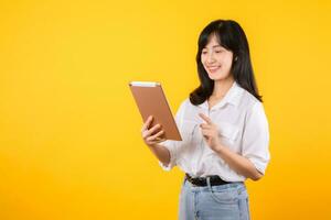 jovem ásia mulher vestindo branco camisa sorrisos brilhantemente enquanto segurando digital tábua contra amarelo fundo, representa uma confiante companhia trabalhador abraçando moderno tecnologia conceitos. foto