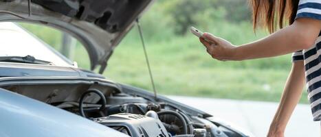 avaria, carro quebrado, reparação. mulher usa telefone celular verifica prêmios de seguro por meio de aplicativo devido a acidente de carro. encontre garagem para consertar o carro durante a turnê pelo país, esperando por ajuda, emergência. foto