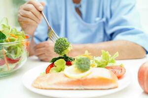 ásia idosos mulher paciente comendo salmão estaca e vegetal salada para saudável Comida dentro hospital. foto