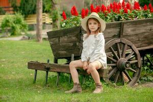 pré-adolescente menina sentado em vintage de madeira carrinho projetado Como canteiro de flores ao ar livre foto