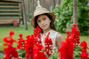 cabelos escuros interpolação menina dentro vime gorro posando perto vermelho flores dentro jardim foto