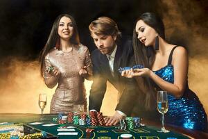 dois lindo mulheres e jovem homem jogar em pôquer mesa dentro cassino, foco em homem e morena foto
