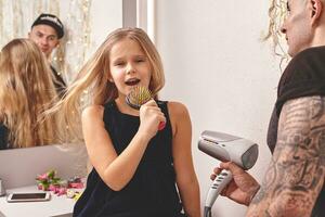 fofa pequeno filha e dela tatuado Papai estão jogando juntos perto uma espelho. Papai é fazendo dele da filha cabelo. família feriado e união. foto