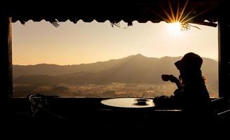jovem mulher asiática sentada no quarto do hotel perto da janela, olhando a vista da montanha e beber café da manhã. turismo e conceito de férias foto