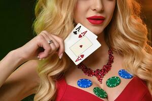 menina dentro vermelho vestir. mostrando dois verde salgadinhos e alguns colorida em dela decote, segurando dois ases, posando em colorida fundo. pôquer, cassino foto