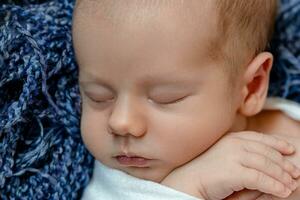 recém-nascido - bebê, face fechar-se. a dormindo recém-nascido Garoto debaixo uma branco tricotado cobertor mentiras em a azul pelagem. foto