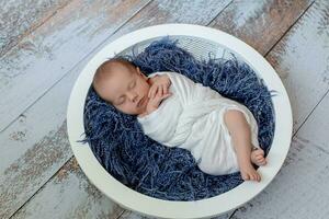 pequeno bebê Garoto dormindo dentro uma cesta em a de madeira chão, estúdio tiro foto