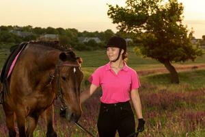 lindo jovem menina sorrir às dela cavalo vestir uniforme concorrência ao ar livre retrato em pôr do sol foto