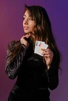 morena mulher dentro Preto veludo vestir mostrando dois jogando cartões, posando contra coloful fundo. jogos de azar entretenimento, pôquer, casino. fechar-se. foto