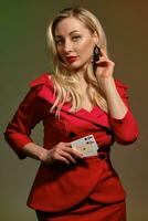 Loiras modelo dentro vermelho à moda vestir. ela tocante dela Preto brinco, mostrando dois jogando cartões, posando em colorida fundo. pôquer, casino. fechar-se foto