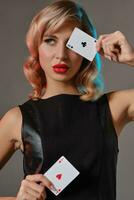 Loiras menina dentro Preto couro vestir mostrando dois jogando cartões, posando contra cinzento fundo. jogos de azar entretenimento, pôquer, casino. fechar-se. foto