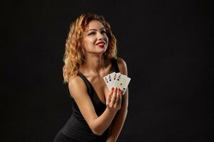 gengibre menina vestindo uma Sombrio vestir é posando segurando quatro ases dentro dela mãos em pé contra uma Preto estúdio fundo. cassino, pôquer. fechar-se. foto