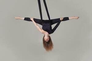 lindo menina dentro uma Preto esporte terno é realizando a acrobático elementos dentro uma estúdio. foto