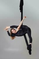 lindo menina dentro uma Preto esporte terno é realizando a acrobático elementos dentro uma estúdio. foto