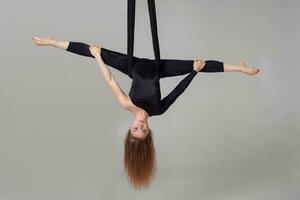 lindo menina dentro uma Preto esporte terno é realizando a acrobático elementos dentro uma estúdio. foto