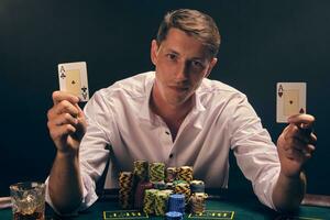 bonito emocional homem é jogando pôquer sentado às a mesa dentro cassino contra uma branco Holofote. foto